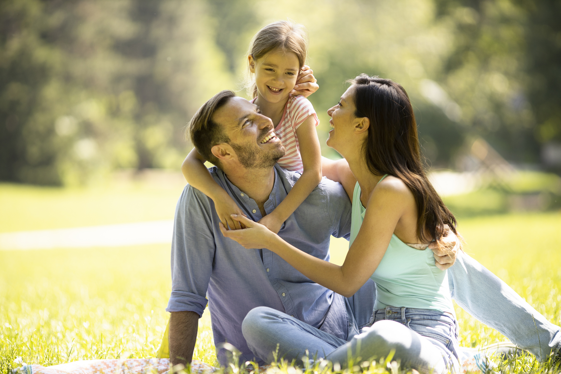 Szczęśliwa młoda rodzina z uroczą córeczką bawiącą się w parku w słoneczny dzień